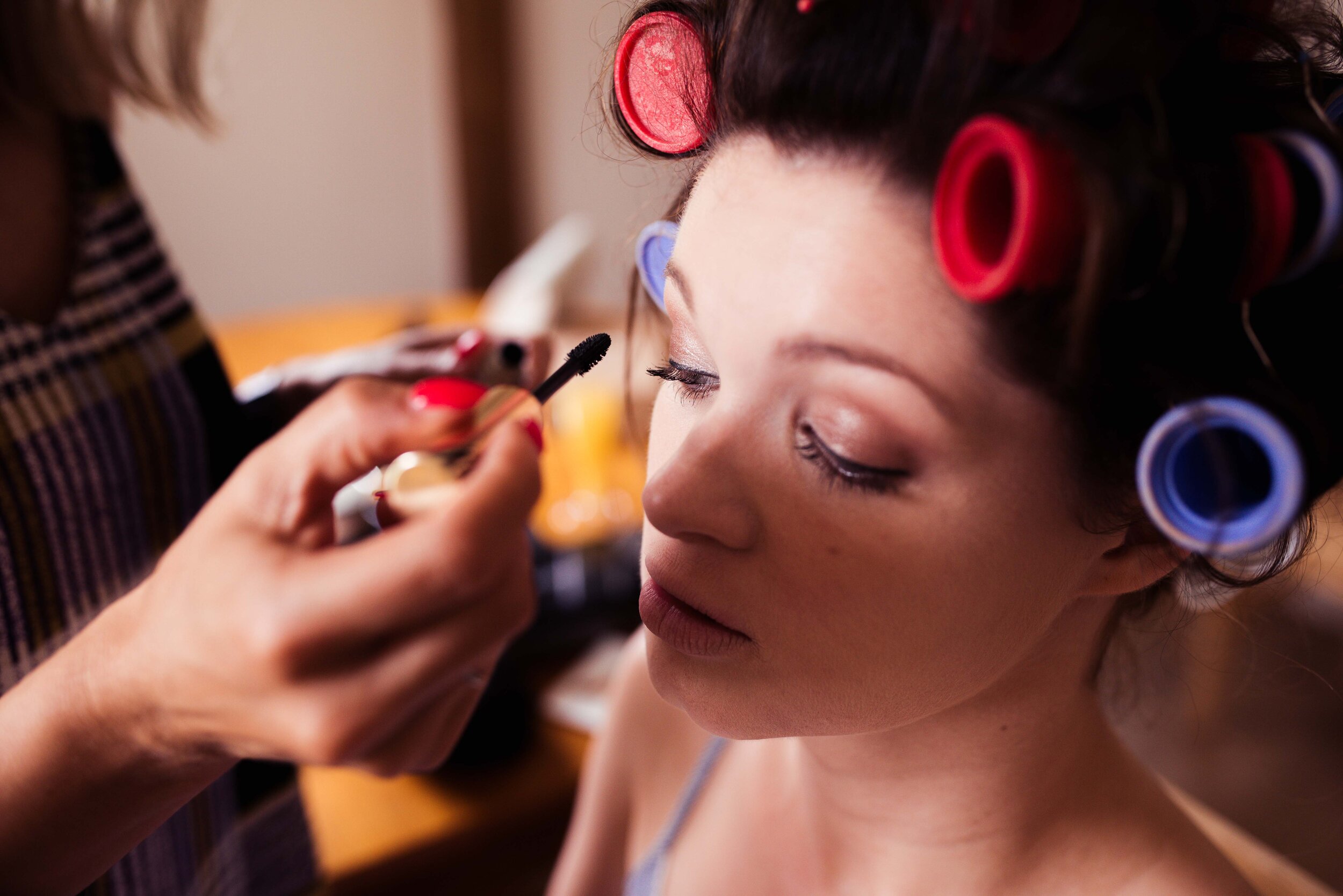 Close up of the bride in hair curlers having her makeup done