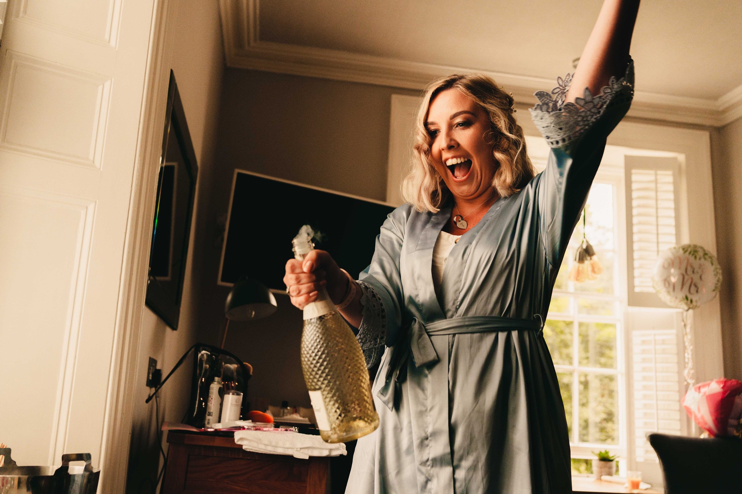 Happy bridesmaid opening a bottle of prosecco