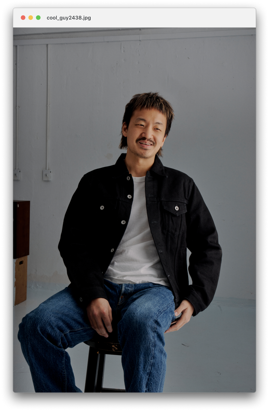 Jordan Leung, wearing a black jacket over a white t-shirt and blue jeans, smiling at the camera.