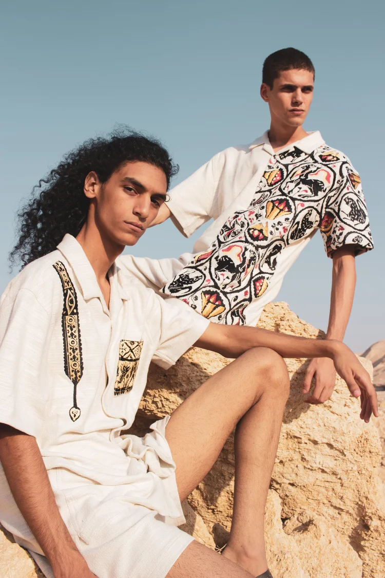 Two men in white shirts with black-and-white prints seated on rocks