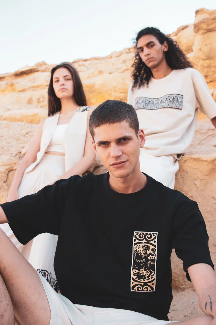 Three models among desert rocks, the man in front in a black T-shirt with a printed panel