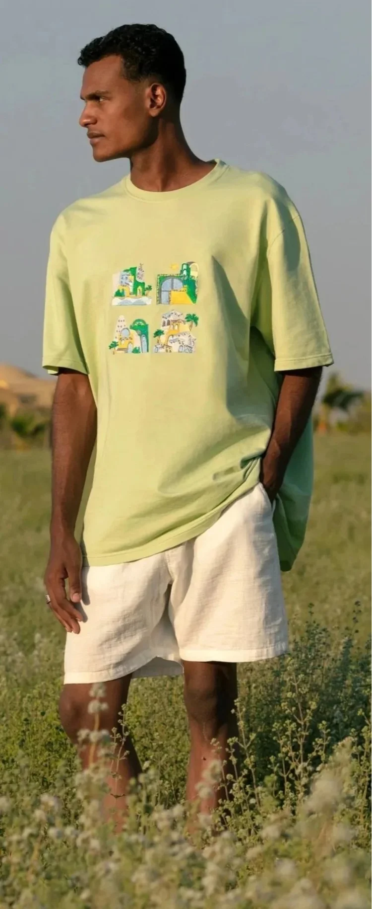 A man in a green graphic T-shirt and white shorts standing in tall grass