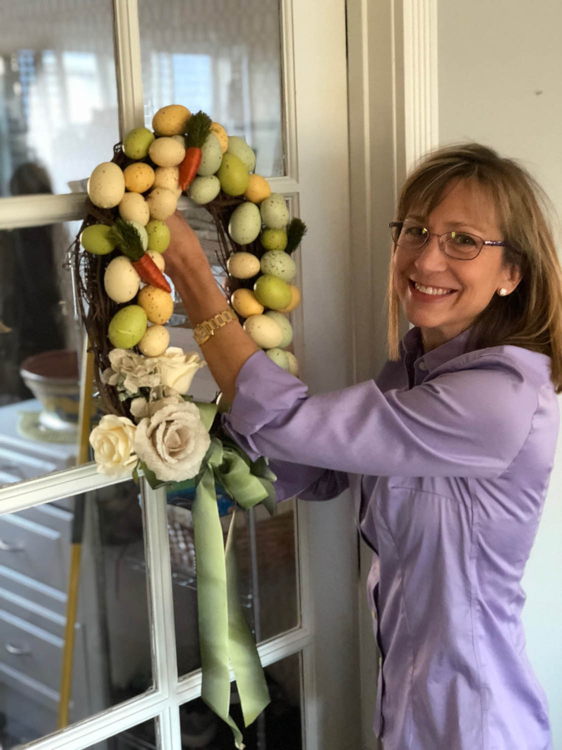 Ashley hangs up the hand made Easter egg wreath on a paned glass door