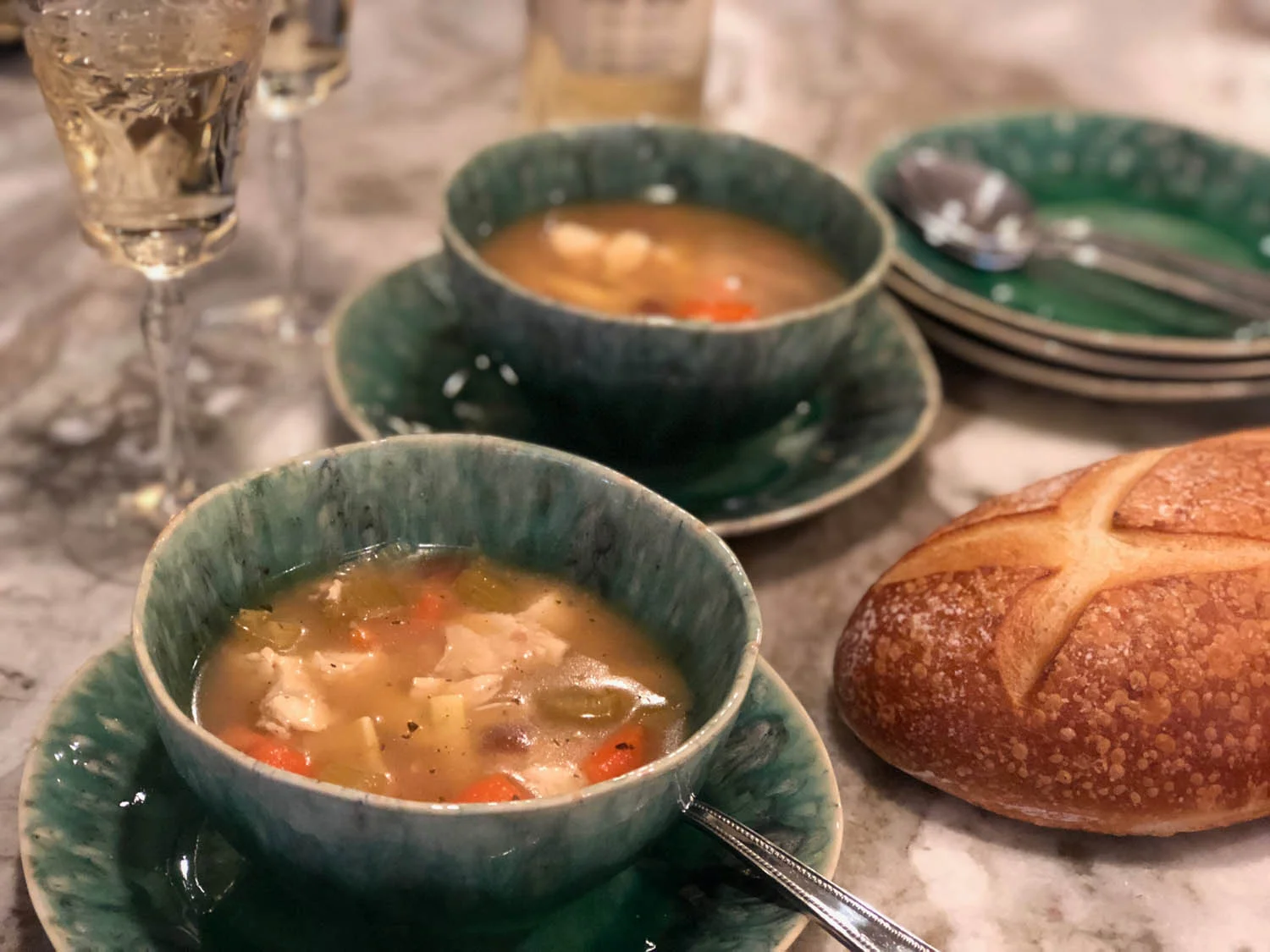 Homemade chicken noodle soup served in bowls with french bread and wine.