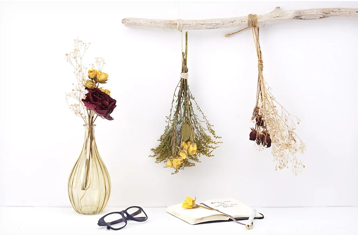 Dried flower bundles displayed in a vase and hanging from a stick hung on the wall.