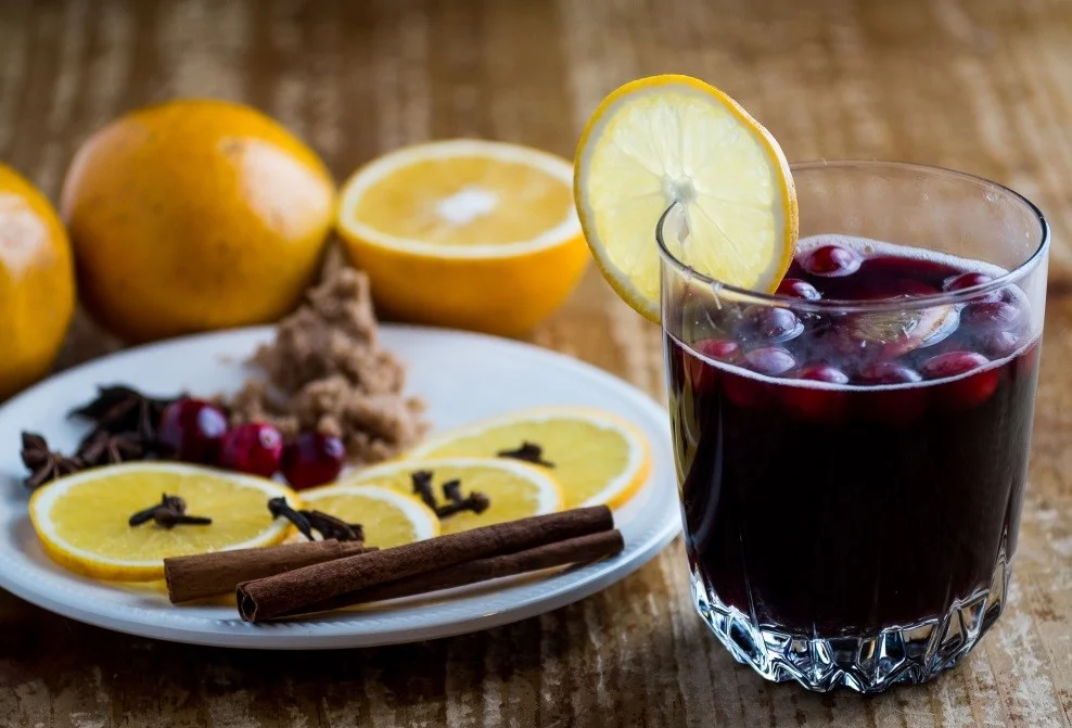 Mulled wine in a clear glass with floating berries garnished with an orange slice