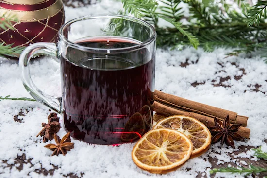 Mulled wine in a glass mug with cinnamon sticks and orange slices on snow.