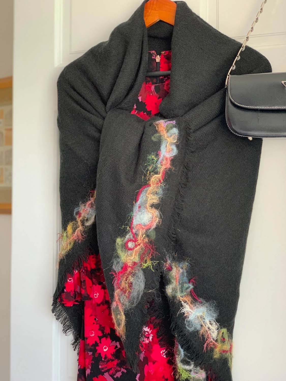 Needle felted fibers embellishing the border of a pre-made shawl wrap over a dress hanging on a door
