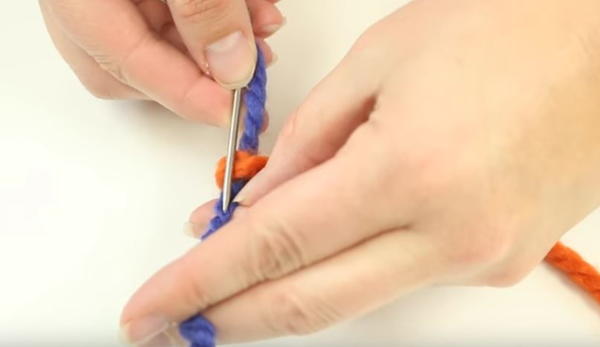 Using a tapestry needle to thread end of yarn back into plies