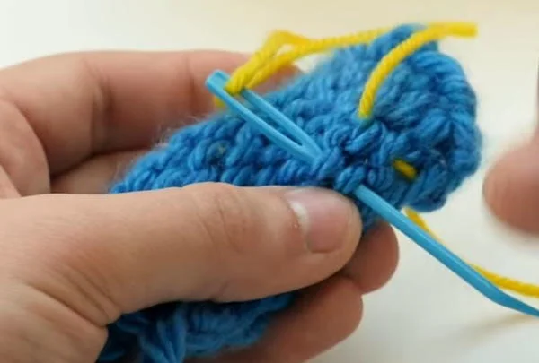 tapestry needle pulling yarn end through knitted loops