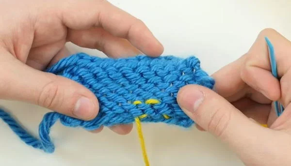 yellow yarn end demonstrating weaving yarn end through back side of knitted swatch