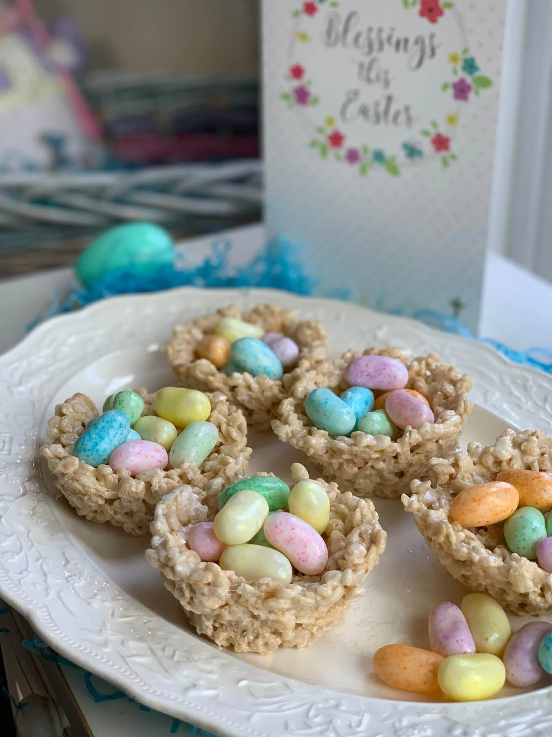 Rice Crispy Treat recipe shaped into nests filled with jelly beans displayed on a white plate with an Easter card