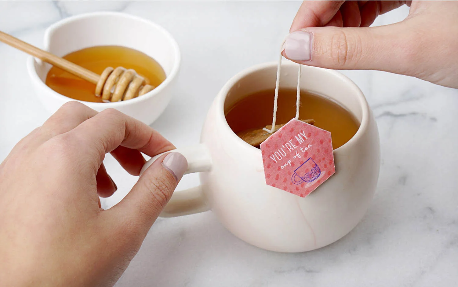DIY tea bag with tag design printed at home steeping in a cup of hot water next to a bowl of honey