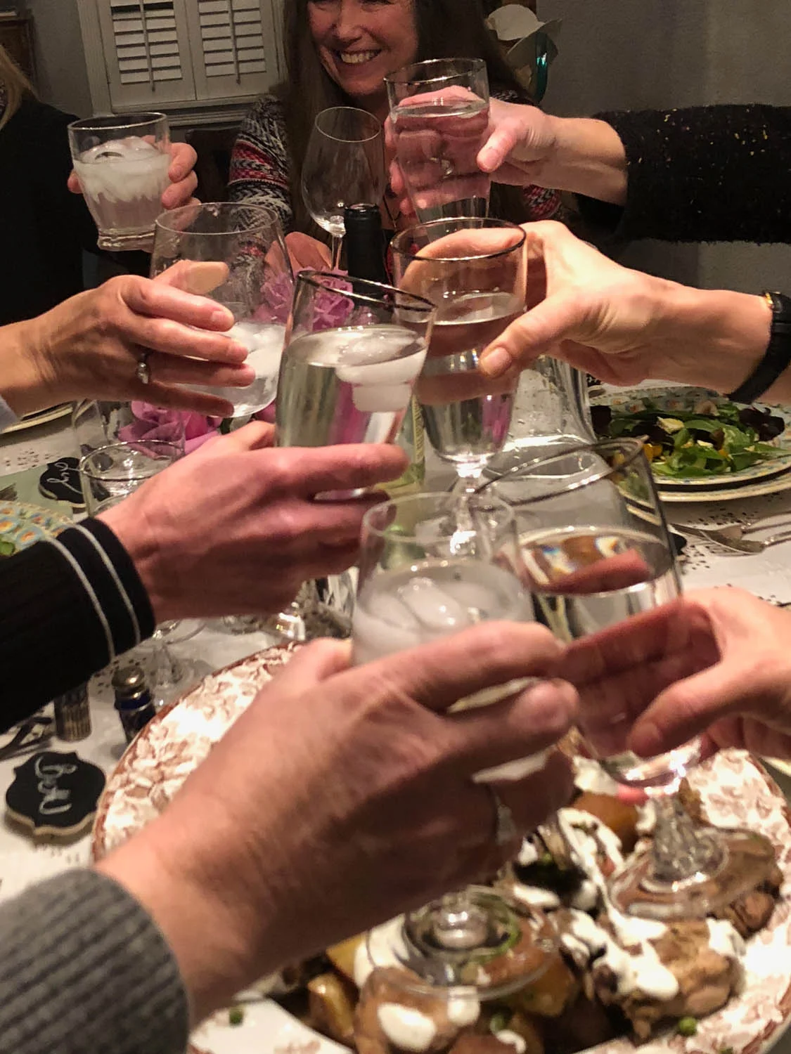 Ladies’ hands toasting goblets over a shared dinner.