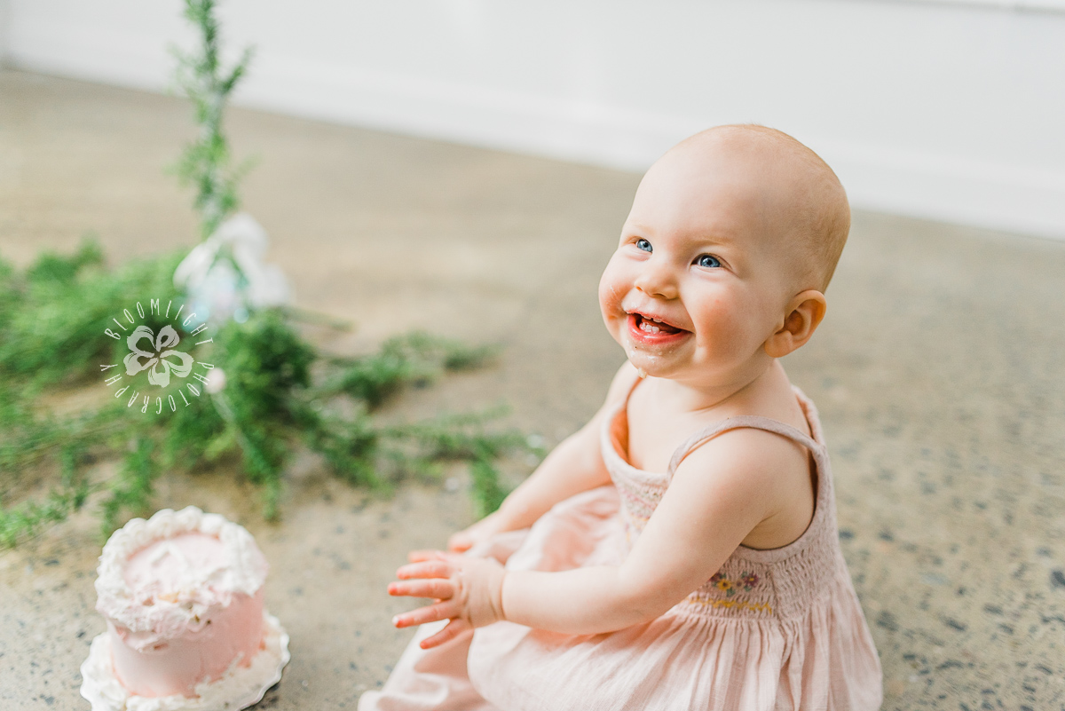 baby girl smiling at her cake smash photo shoot.