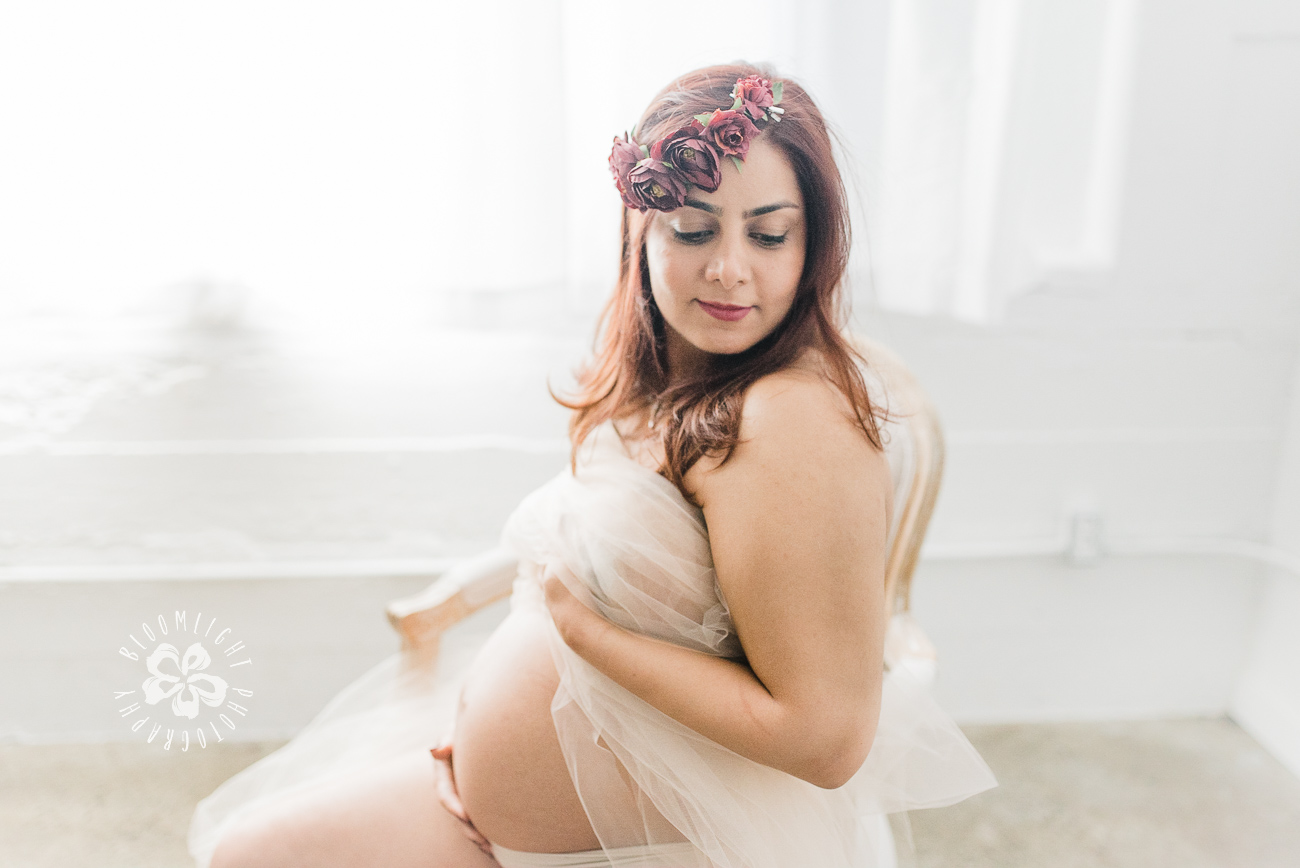 Dreamy picture of pregnant mom in Toronto studio wrapped in tulle sitting on a chair.