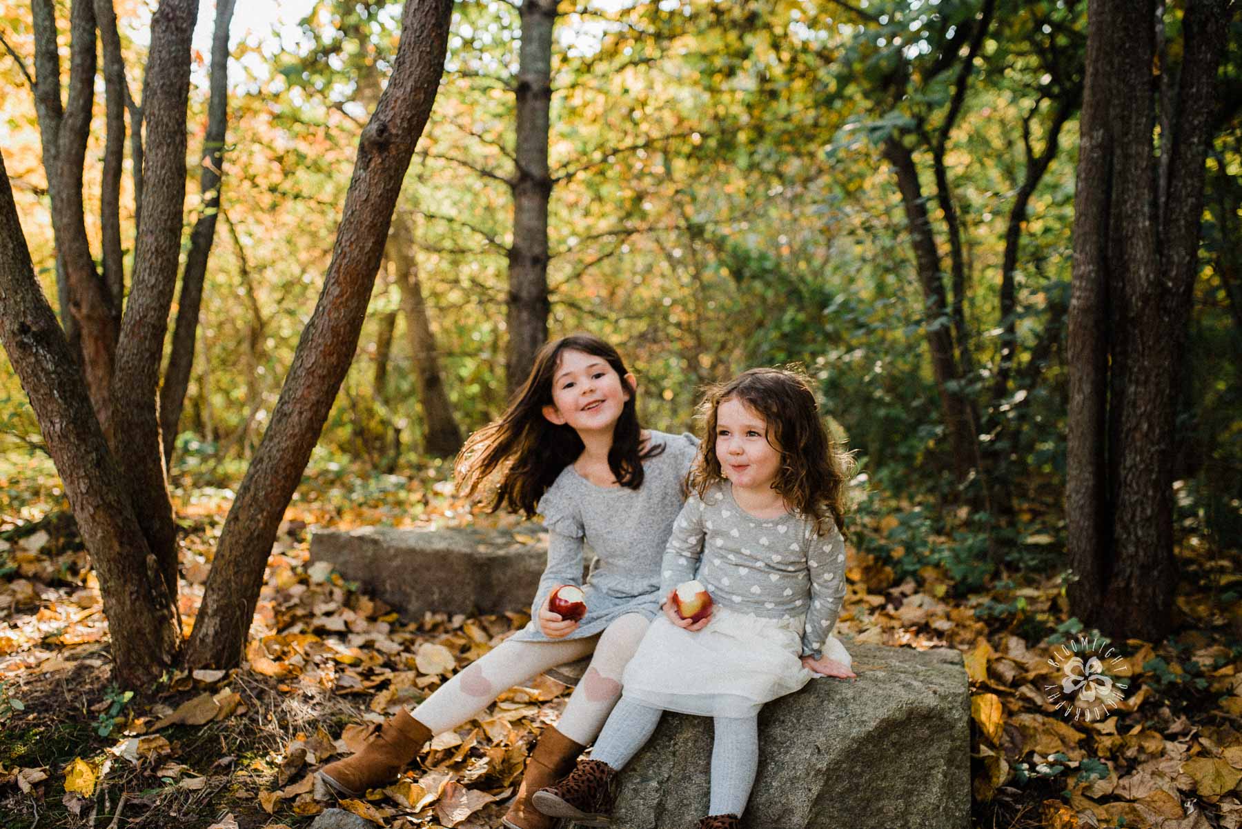 Sisters sitting on a rock in Evergreen Brick works park in Toronto in a colorful Fall.