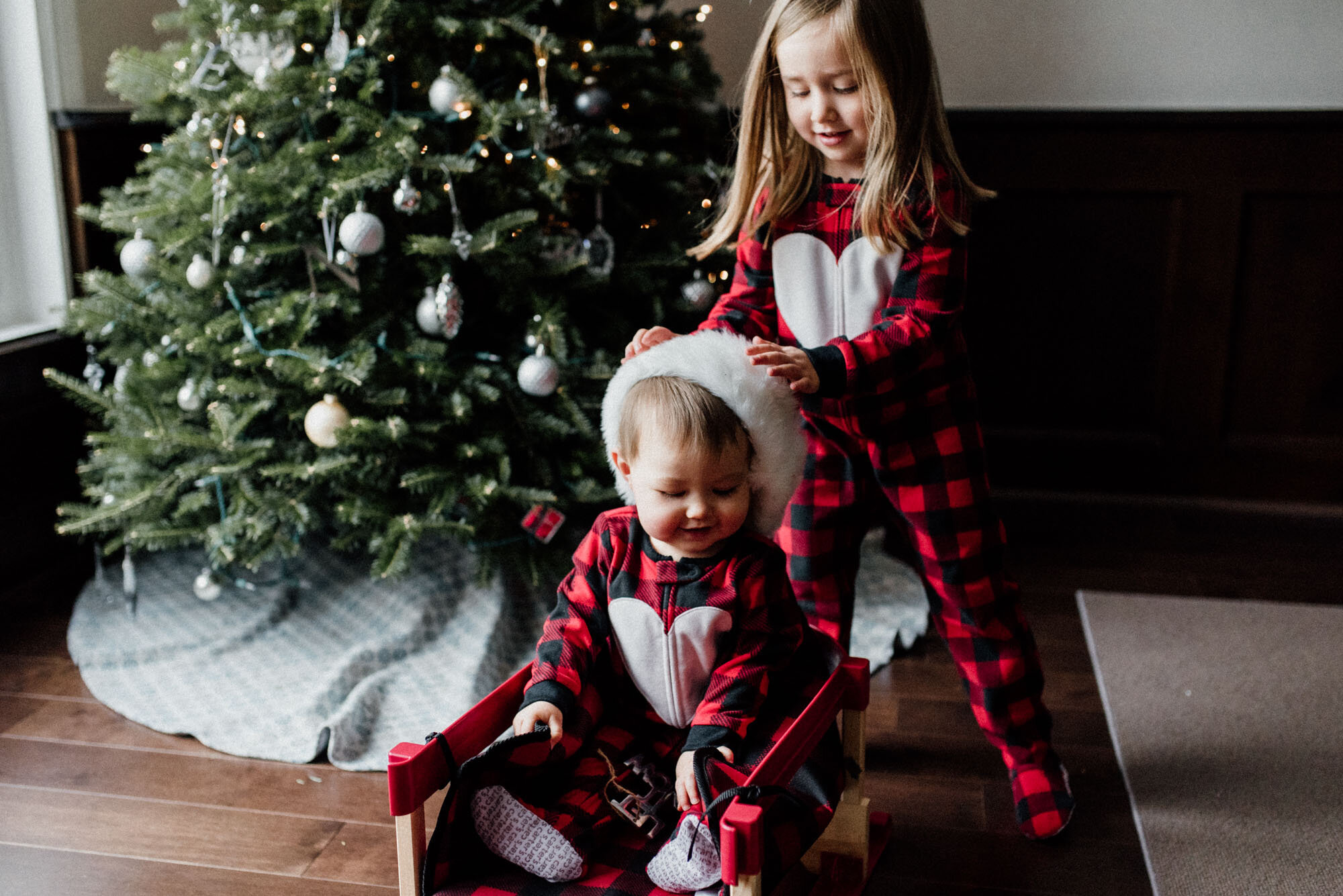 Kids wearing pjs playing with Santa hat in front of the Christmas tree at home