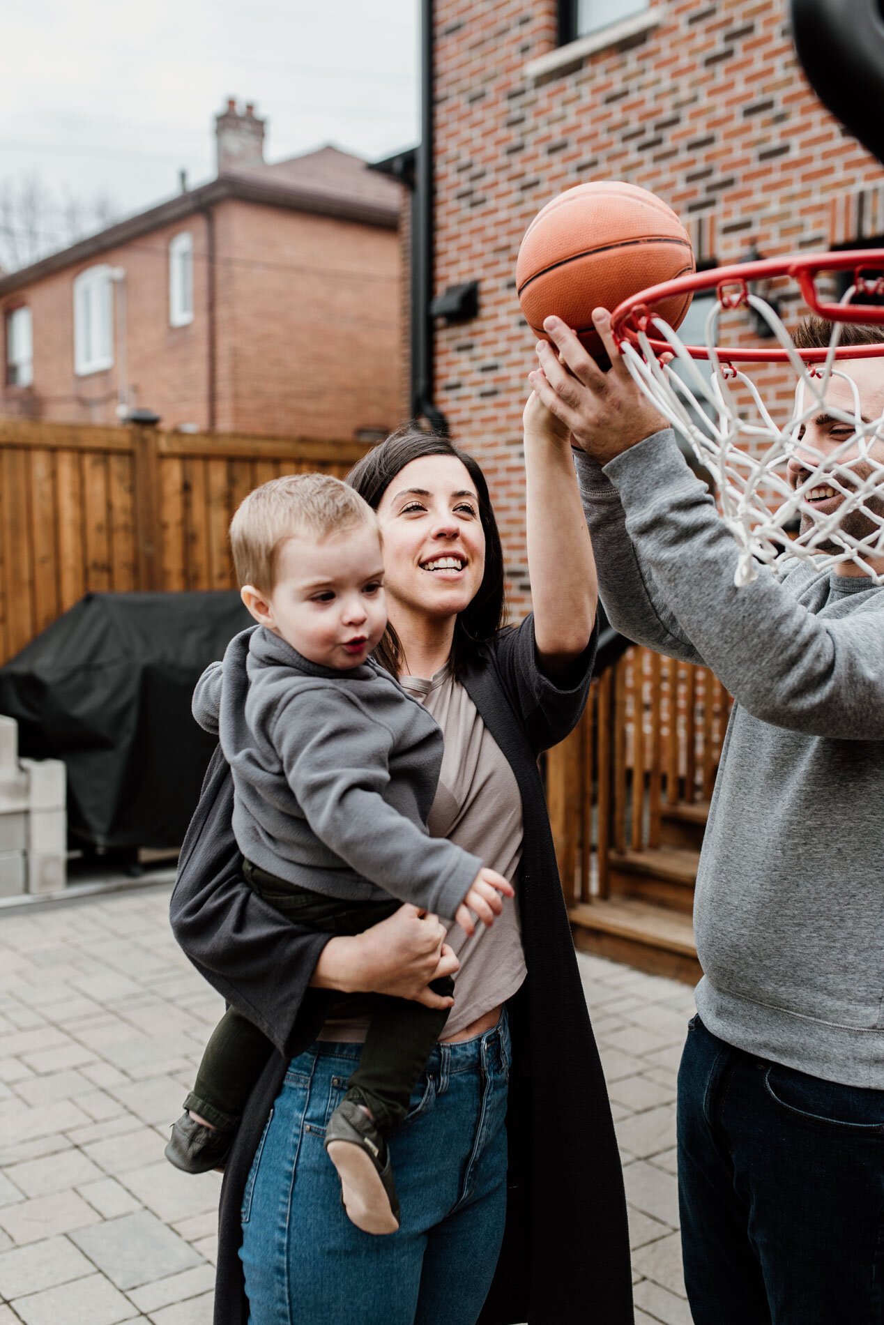 baby boy and her mom are throwing ball into basketball net 