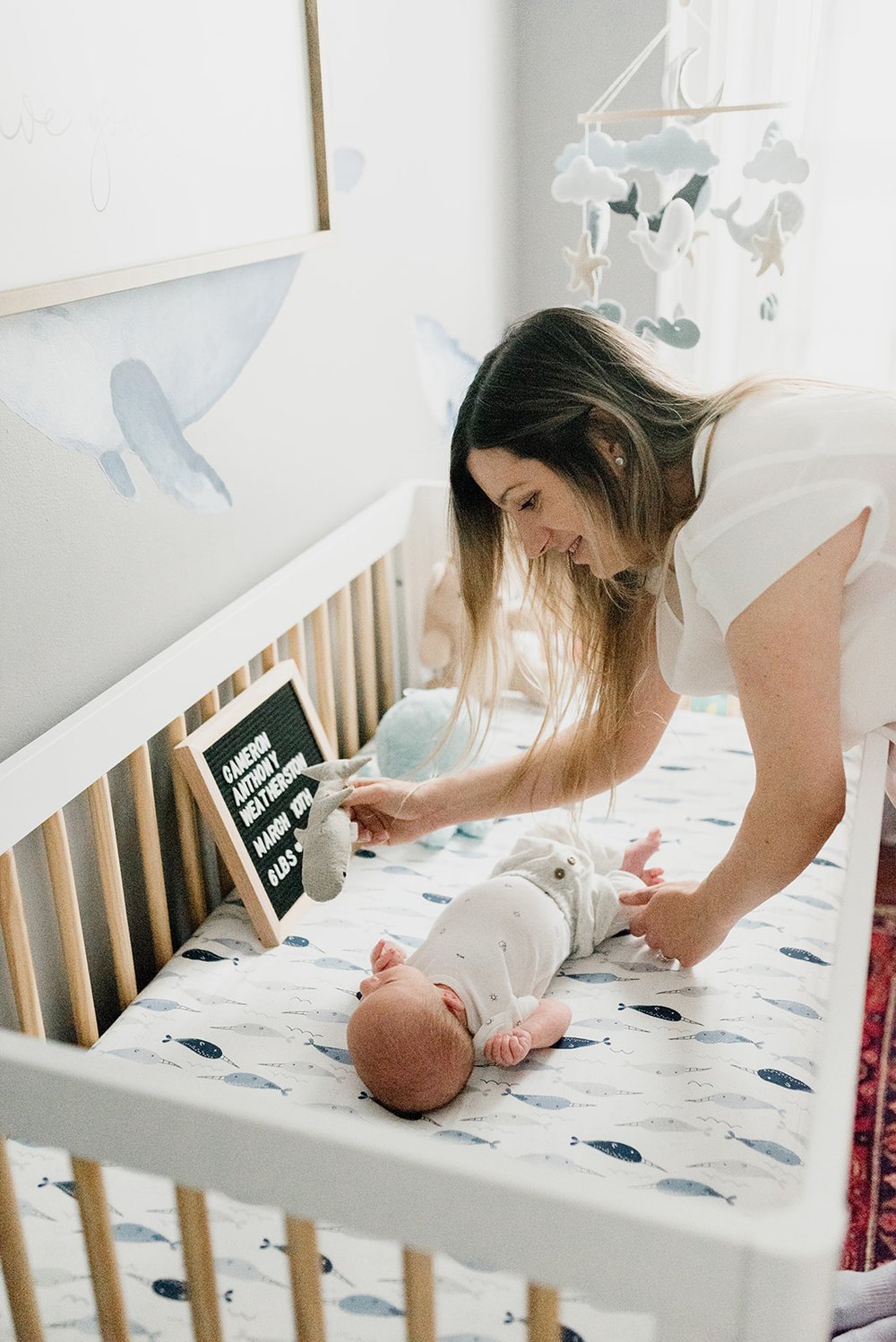 Picture of a mom making her newborn calm in the crib in the beautiful Sea theme nursery in Toronto