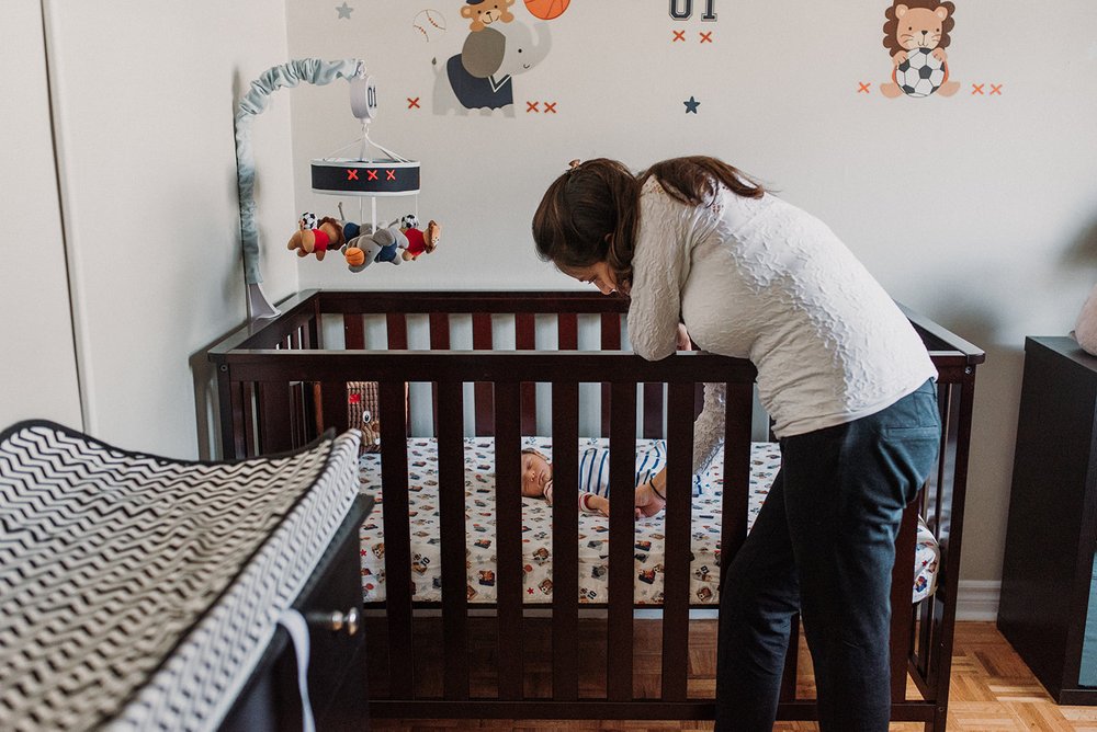 new mom making her newborn comfortable in her crib in his sport theme nursery