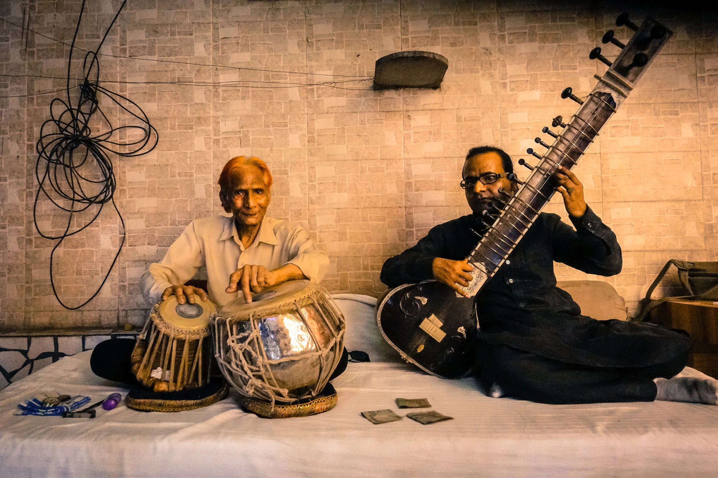 Man to the left playing tabla drums and man to the right playing a sitarr (like) instrument. Agra, 2017.