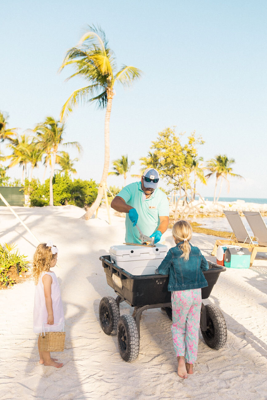  A staff member at The Islands of Islamorada prepares a shellfish for two young girls to eat on the beach. 