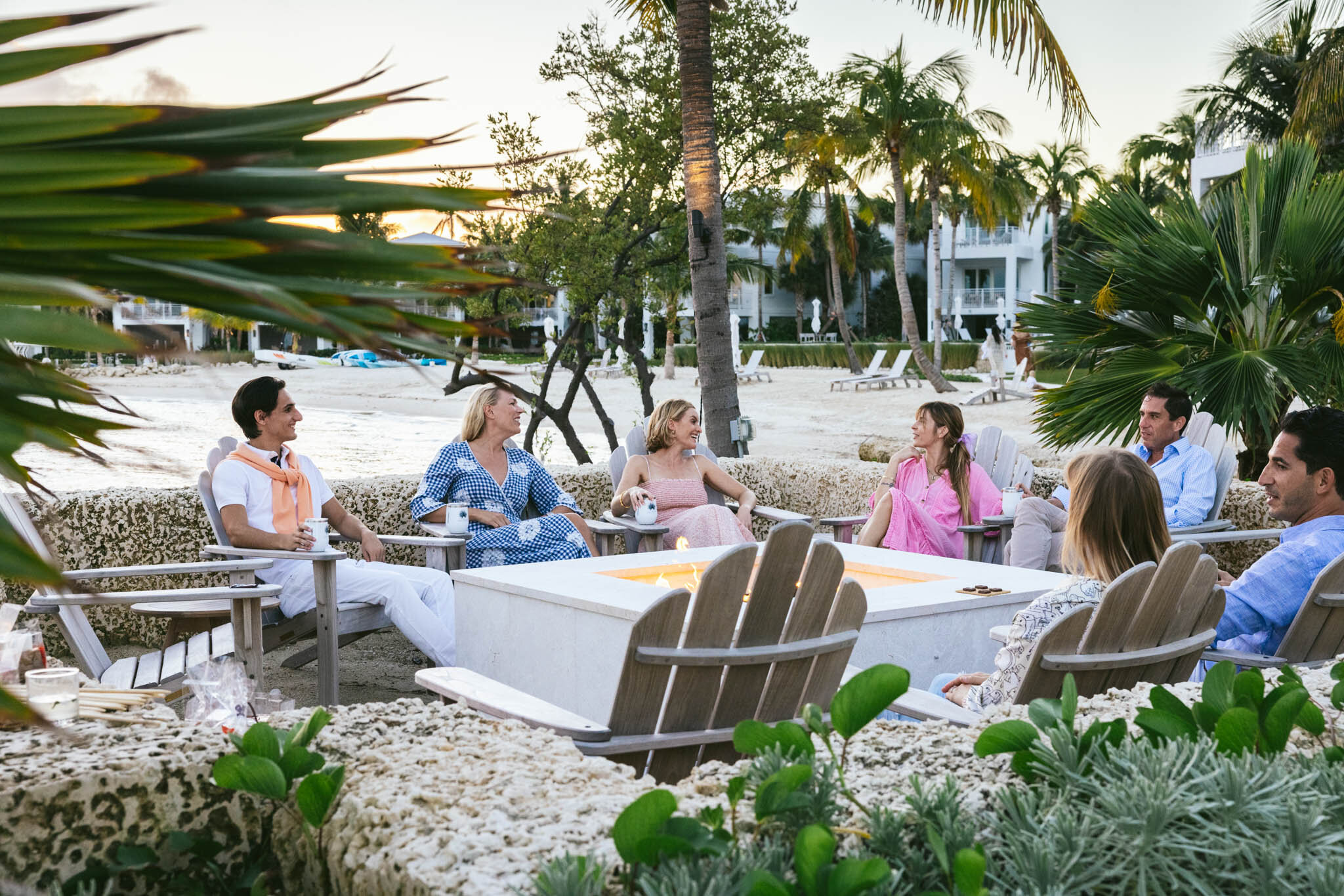  Couples Gathered In Chairs Relax Around A Lit Fire Pit At Dusk On The Islands Of Islamorada’s Private Beach. 