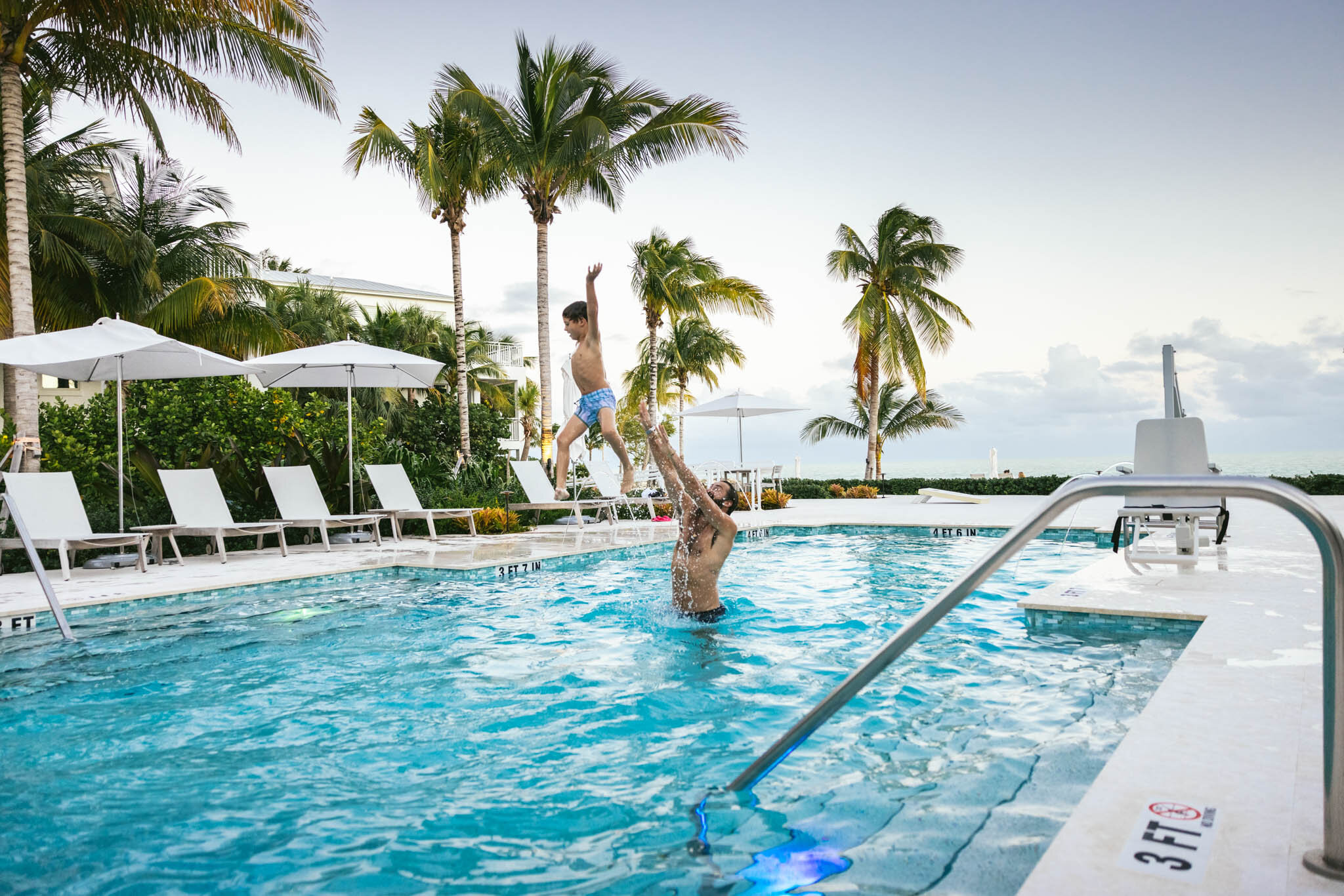  Father Tosses His Son In The Air While Playing In The Islands Of Islamorada’s Private Beachside Pool While On Vacation In Florida.  