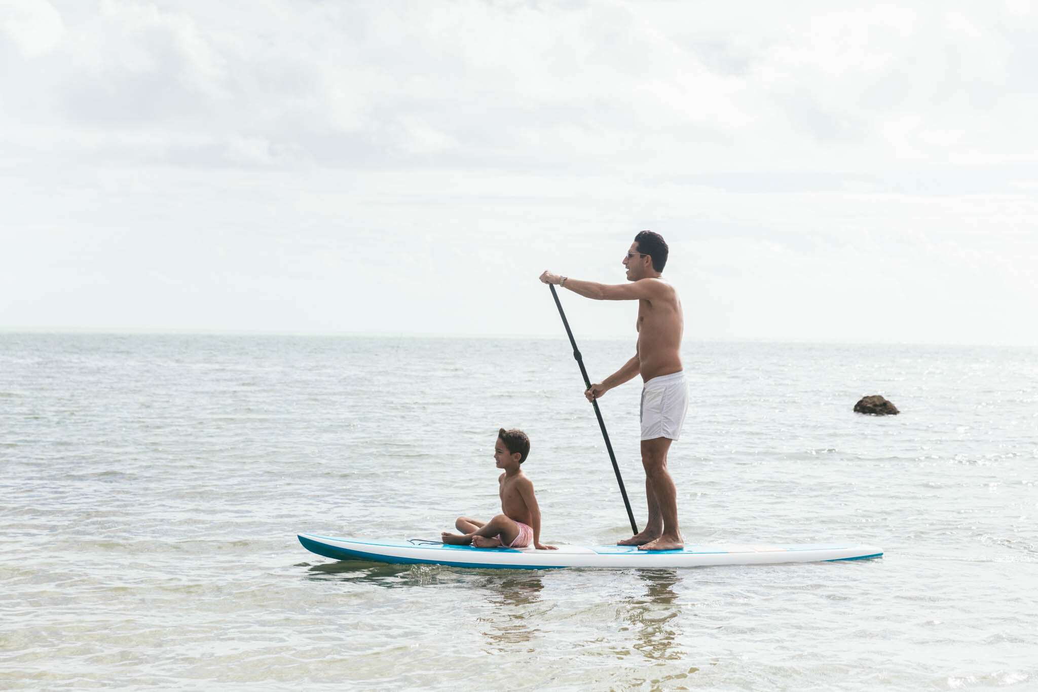  Father Paddleboarding While His Young Son Sits On The Board In The Atlantic Ocean Near The Islands Of Islamorada’s Private Soth Florida Beach.   