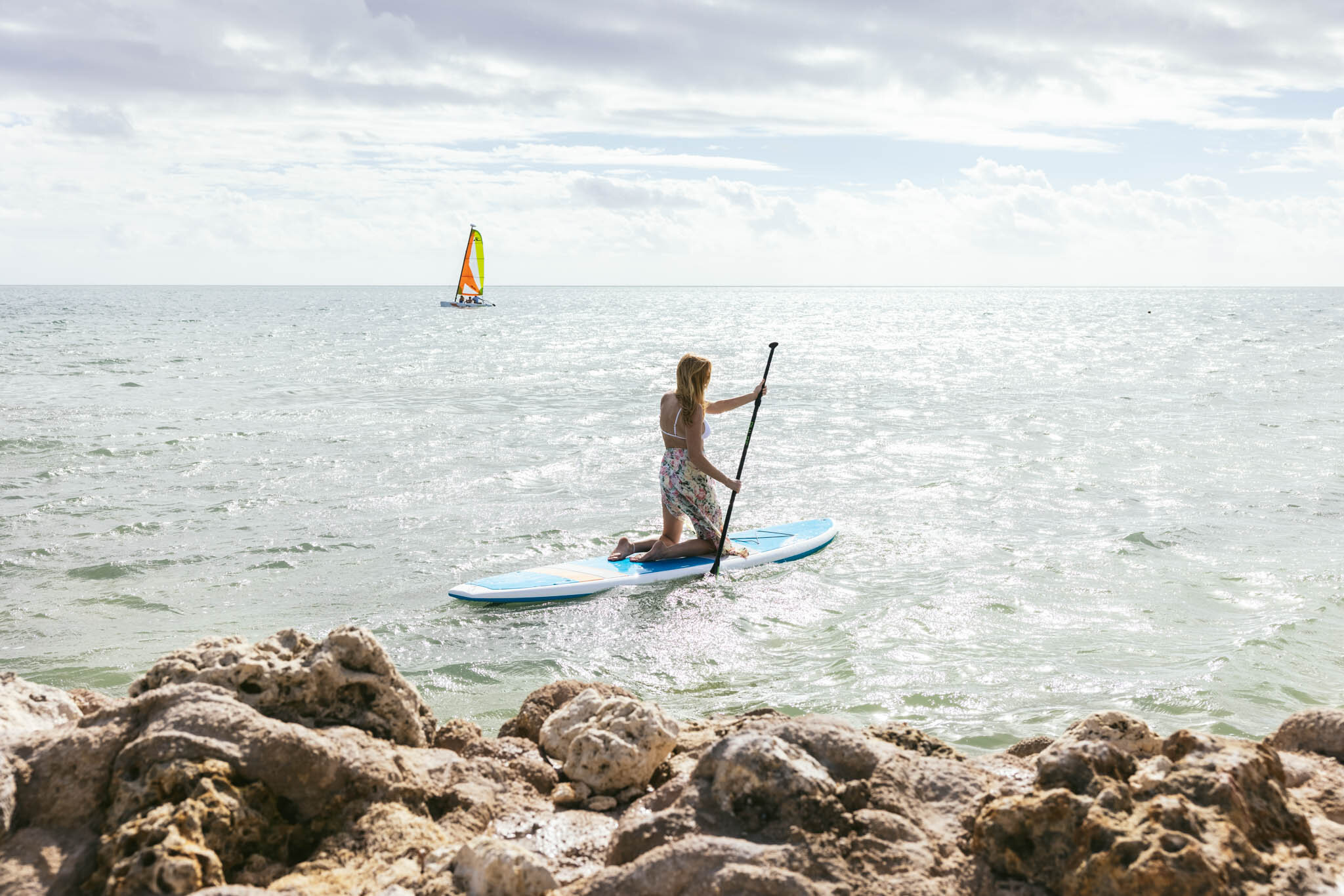  Woman Paddleboarding In The Atlantic Ocean Off The Islands Of Islamorada’s Private Beach, With A Sailboat Farther Out On The Water. 