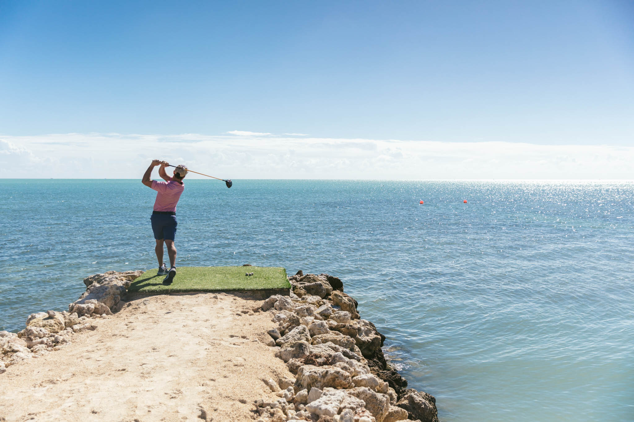  Man Swinging A Golf Club As He Hits A Ball From The Islands Of Islamorada’s Private Jetty Into The Crystal Clear Waters Of The Atlantic Ocean Off The Coast Of Florida. 