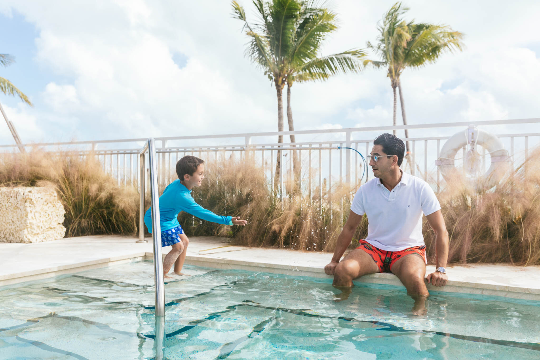  Young boy splashes his dad sitting on the edge of The Islands of Islamorada’s private beachside pool. 