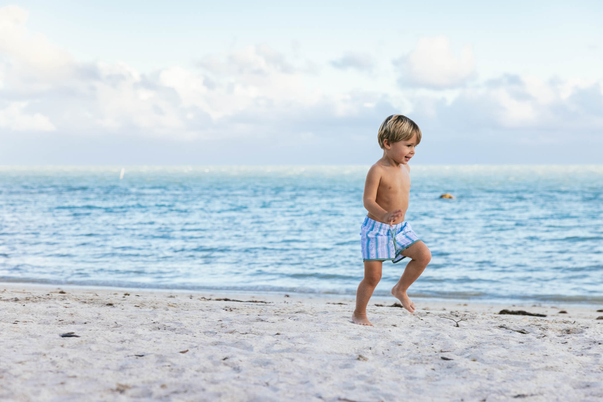  Young boy in swimming trunks running on The Islands of Islamorada’s private beach by the water. 