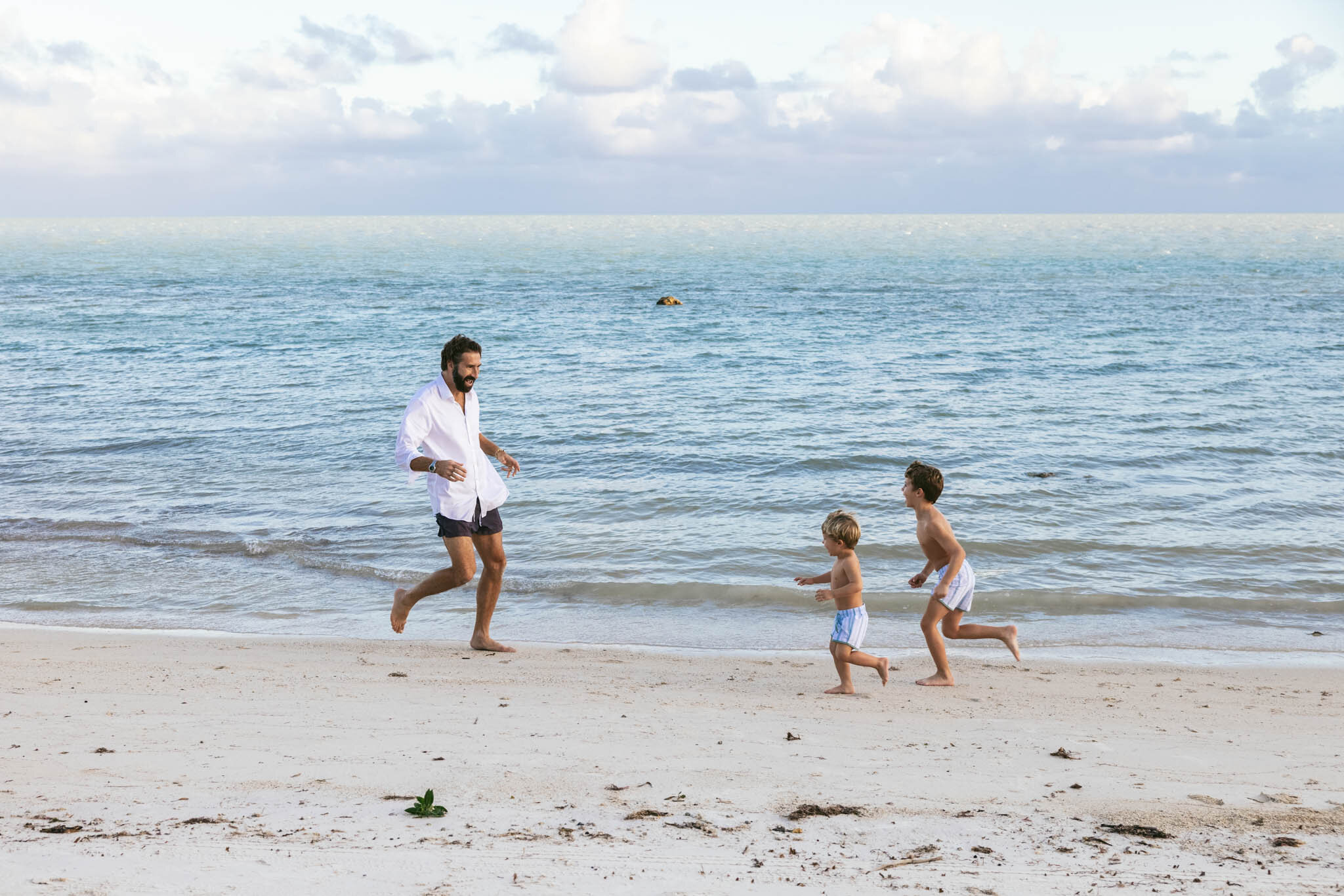  Father and two young sons running on the sand by the water on The Islands of Islamorada’s private beach. 