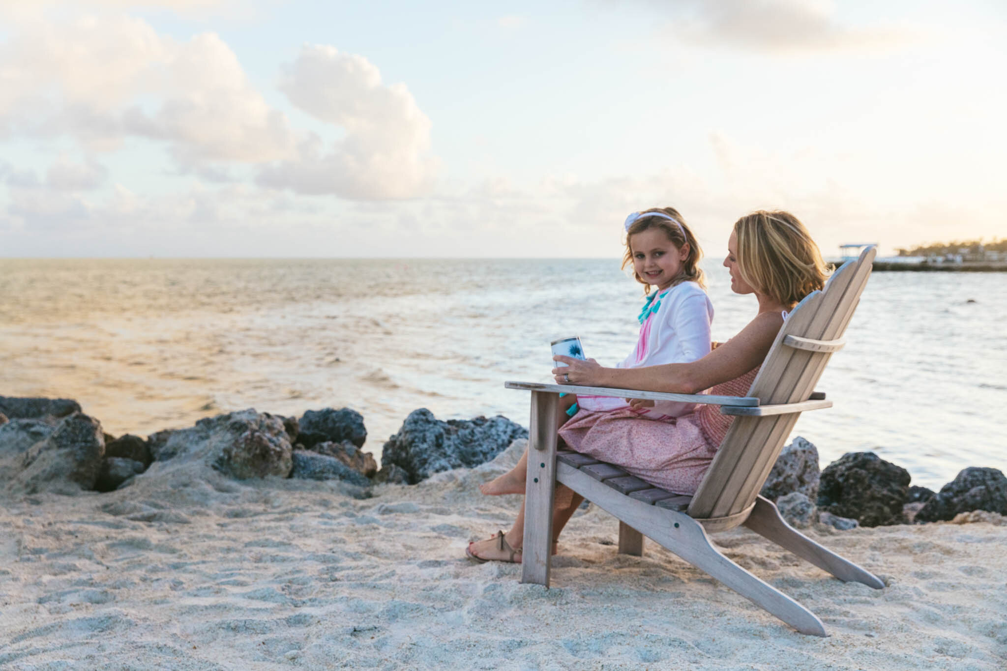  Young girl sitting on her mother’s lap in a beach chair on the sand on  The Islands of Islamorada’s private beach. 
