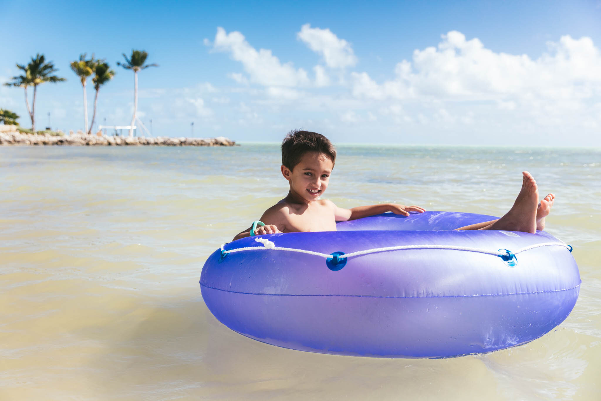  Young boy sits in a swim ring in the crystal clear waters of the Atlantic Ocean on The Islands of Islamorada’s private beach. 