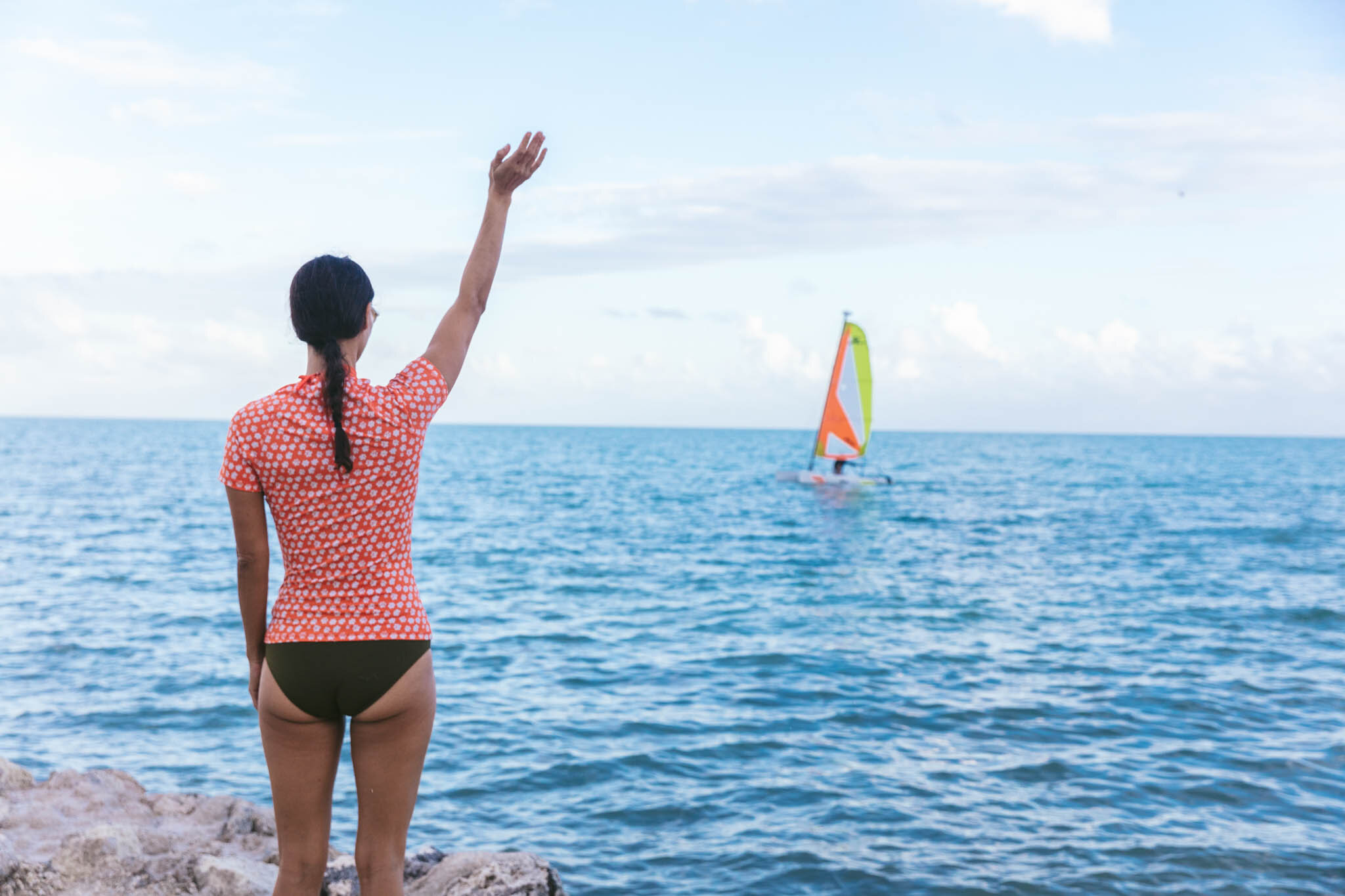  Woman on The Islands of Islamorada’s private beach waves to a sailboat on the crystal clear waters of the Atlantic Ocean. 