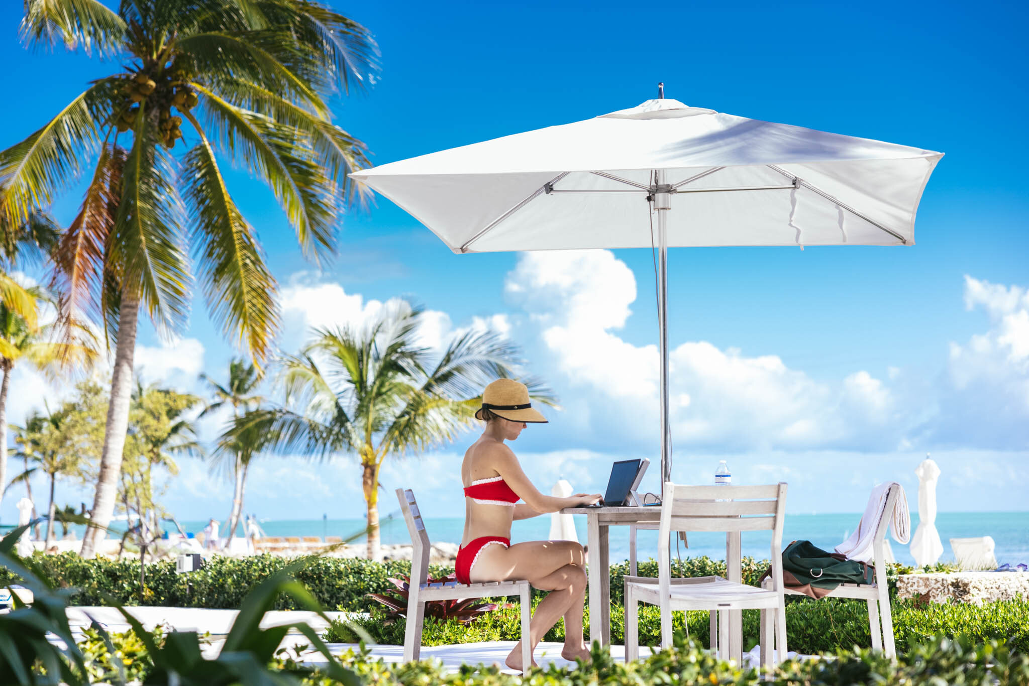  Woman in a swim suit working on a laptop under an umbrella outside at The Islands of Islamorada, next to the resort’s private beach. 