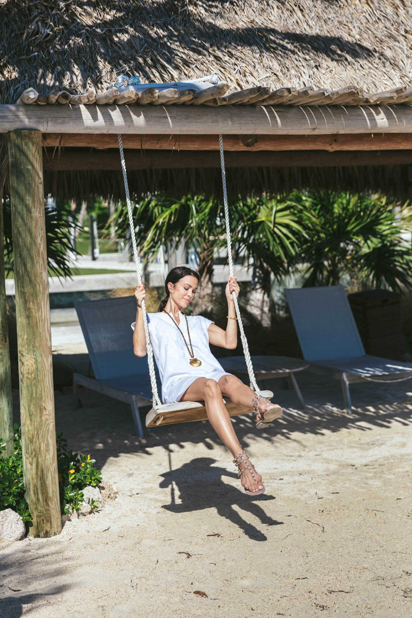  Woman sitting and swinging on a swing under The Islands of Islamorada’s beachside tiki bar hut. 
