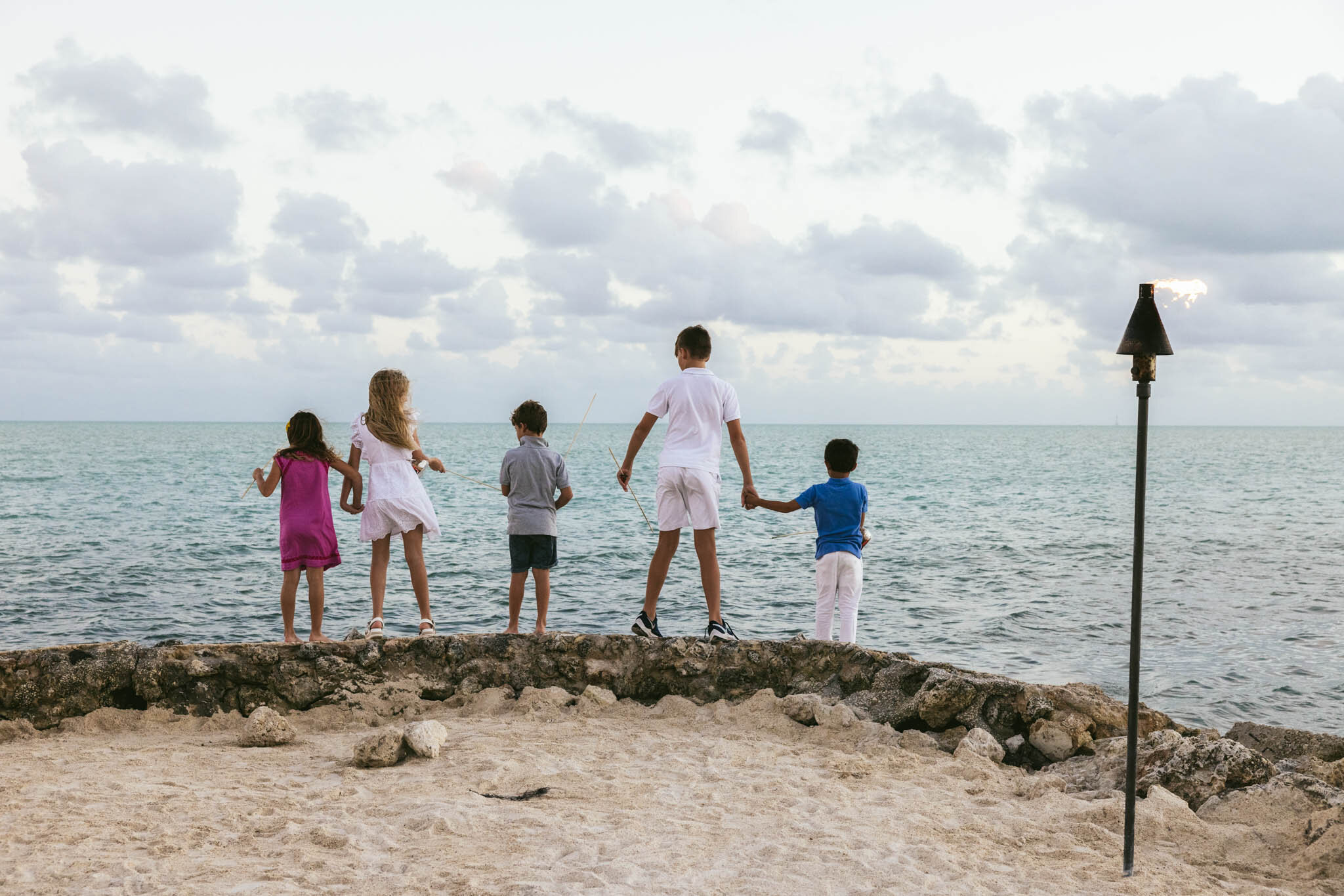  Group of kids holding hands as they stand on the rocky edge of The Islands of Islamorada’s private jetty looking out onto the Atlantic Ocean. 