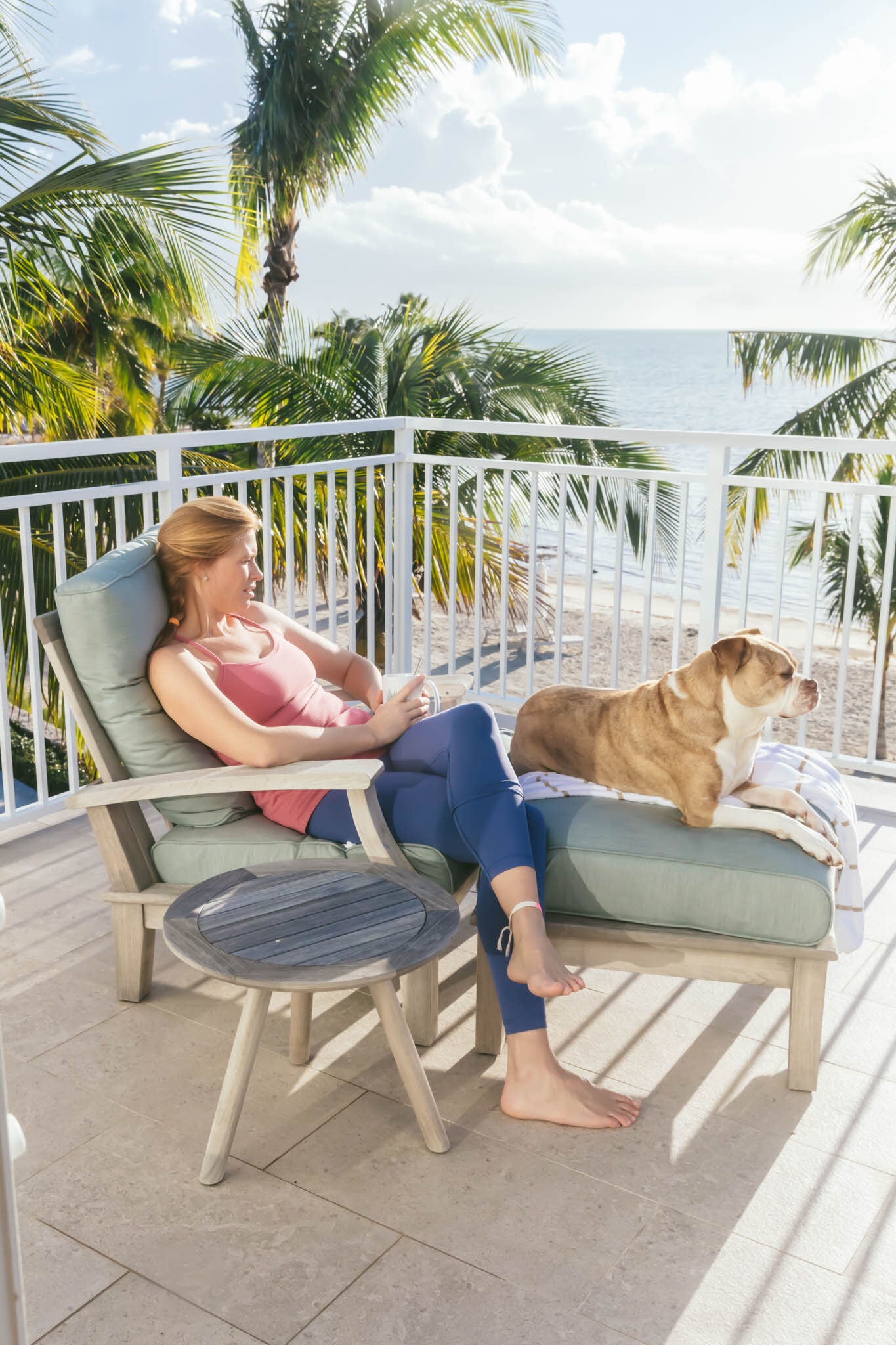  Woman and dog sit on the ocean view balcony of an Islands waterfront villa. 