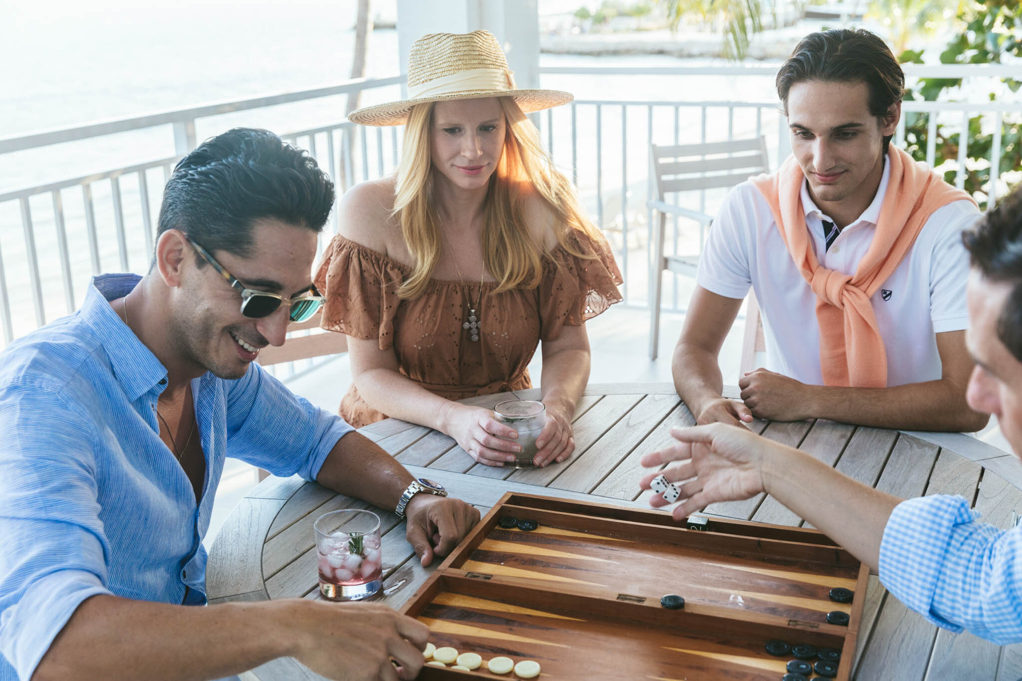  Group of people playing a game of backgammon on the covered balcony of an Islands waterfront villa. 