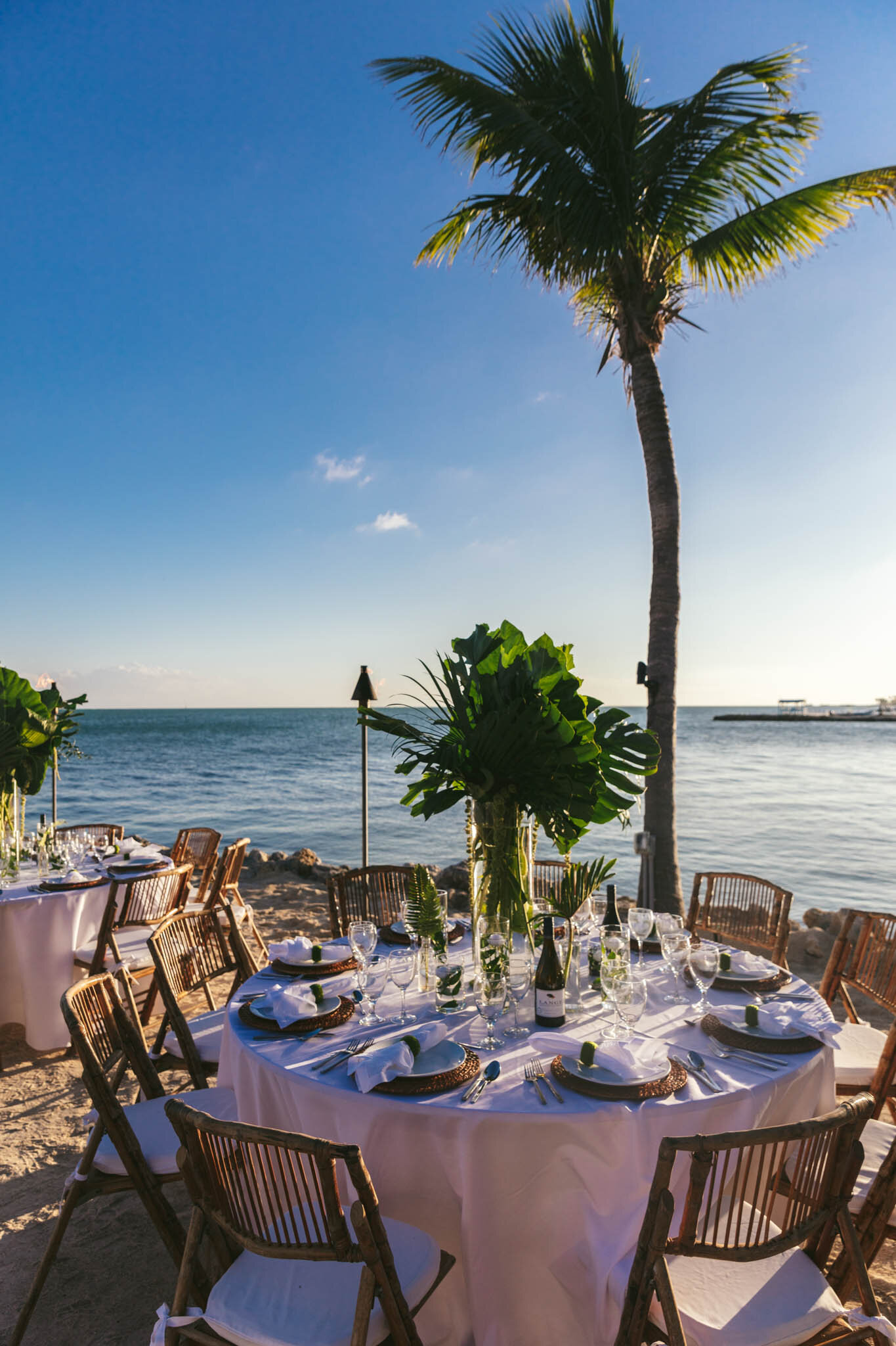  Table set for a wedding reception on the beach under a palm tree on The Islands of Islamorada’s private beach. 