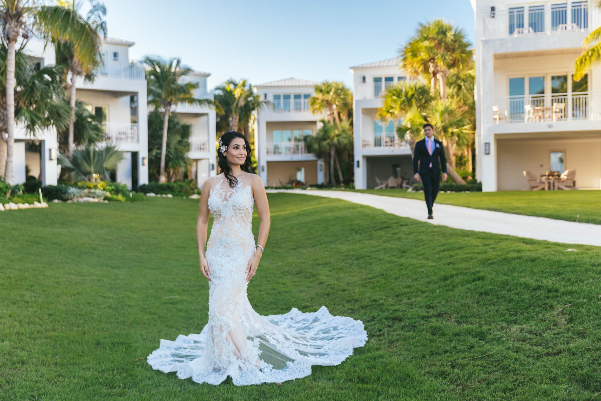  Bride in her wedding dress stands on The Islands of Islamorada’s open lawn as her groom walks up from a row of waterfront villas. 