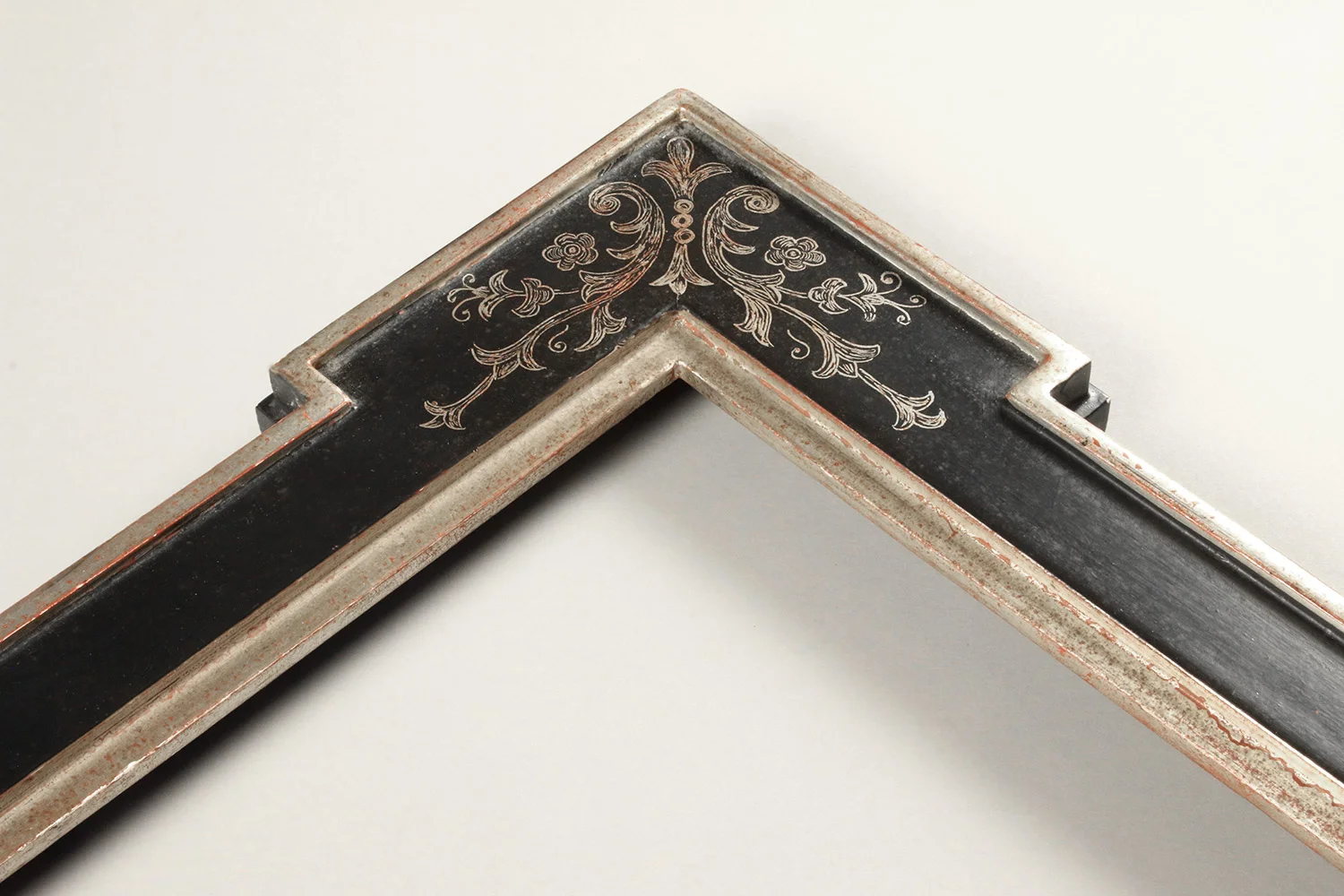 A white gilded frame with a black painted panel with a corner sgraffito design.