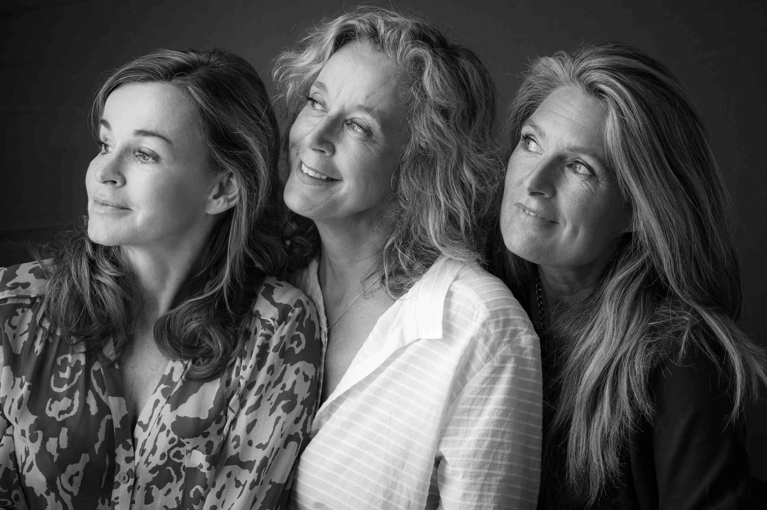 Drie vrouwen kijken omhoog en glimlachen in een zwart-wit foto.