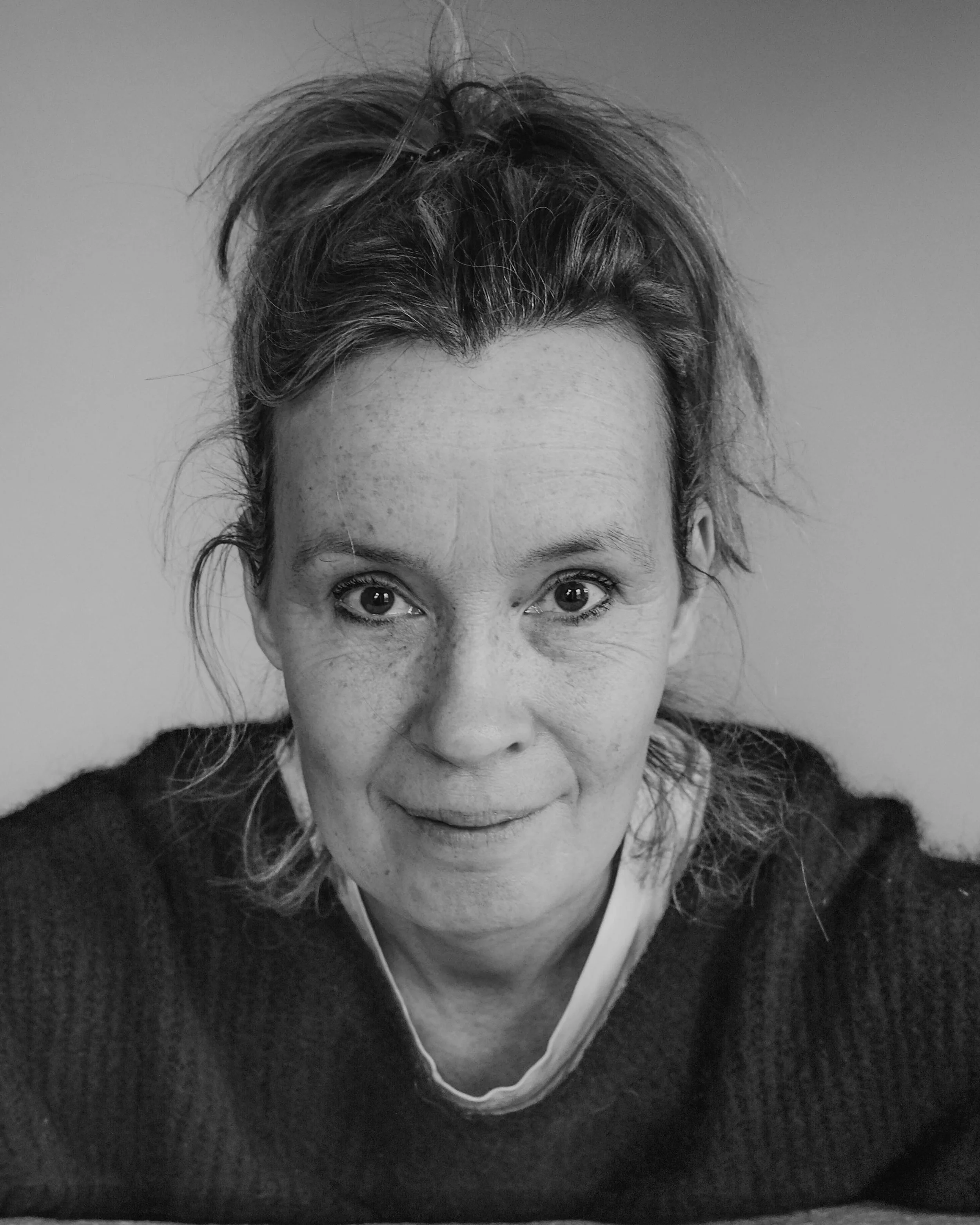 Zwart-wit foto van een vrouw met warrig haar, glimlachend naar de camera, met een neutrale achtergrond.