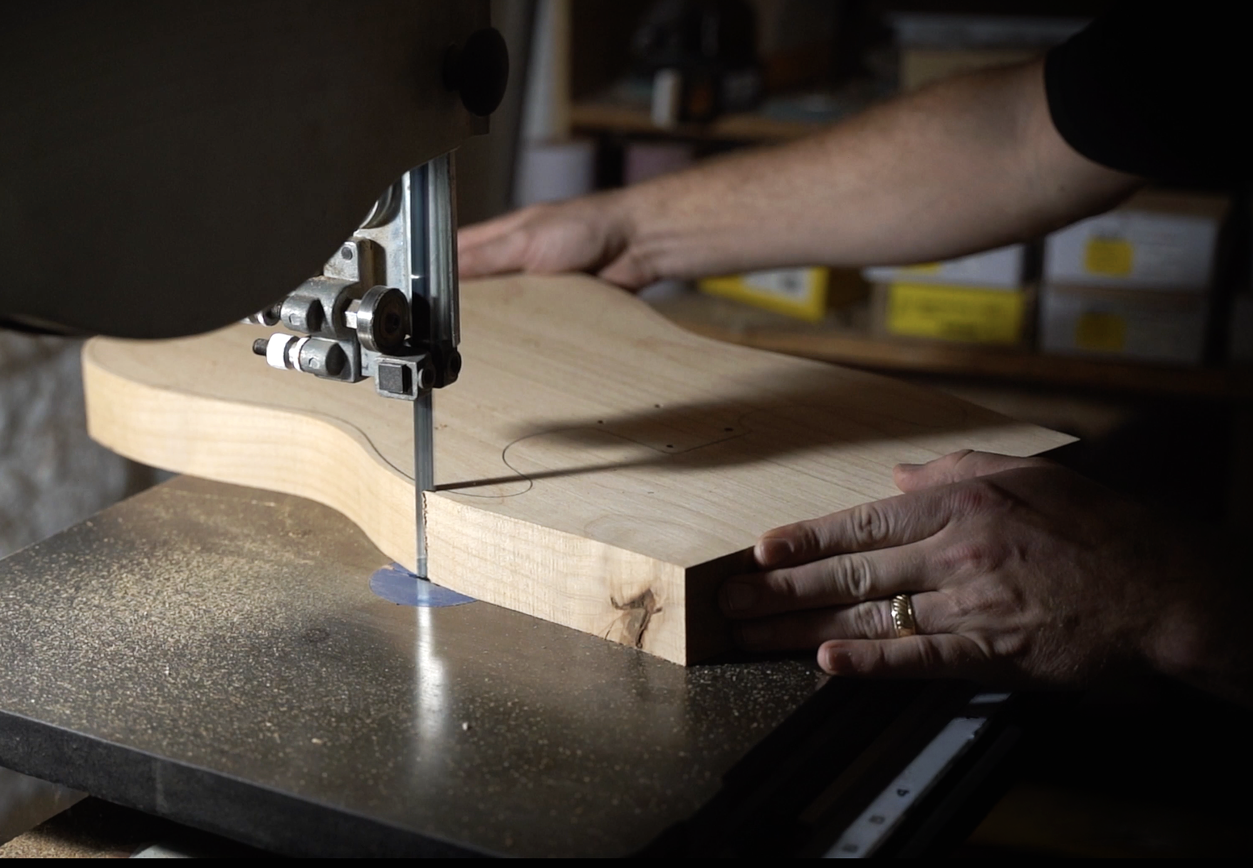 A person operating a bandsaw, cutting a piece of light-colored wood in a workshop.
