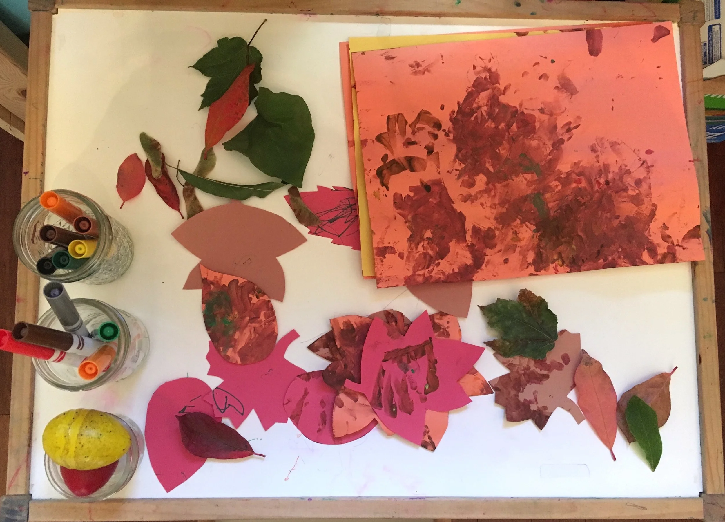Image: an art table with fall leaves, markers, crayons and construction paper